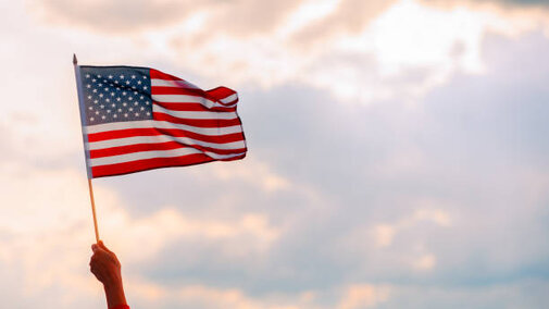 Hand holding US flag against blue sky
